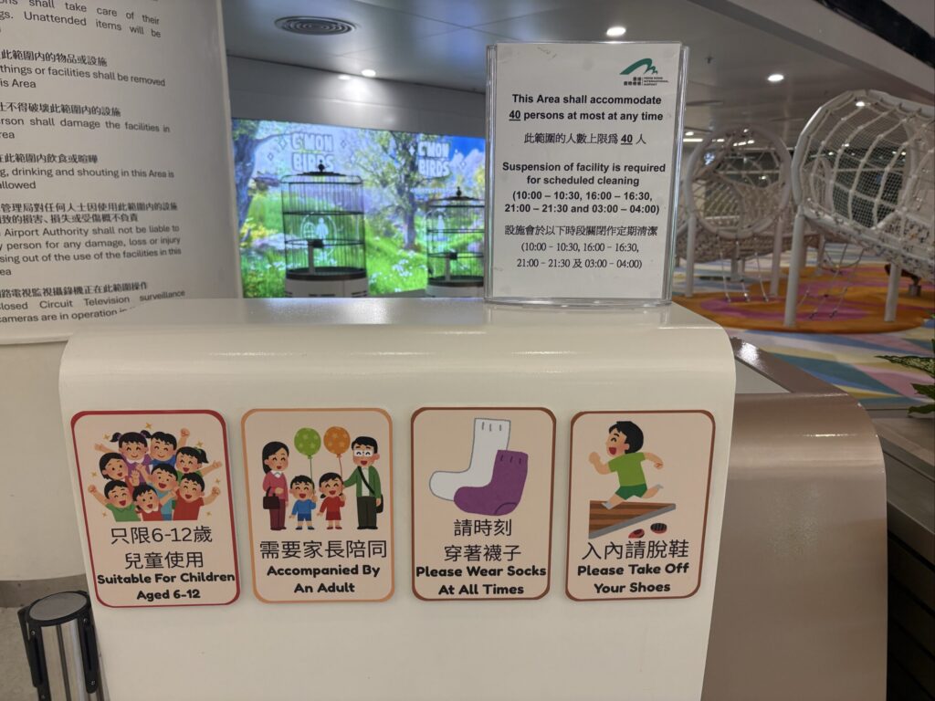 香港国際空港のキッズスペースの案内表示。6〜12歳のみ利用可、保護者同伴、靴を脱ぐ、靴下着用と書かれている