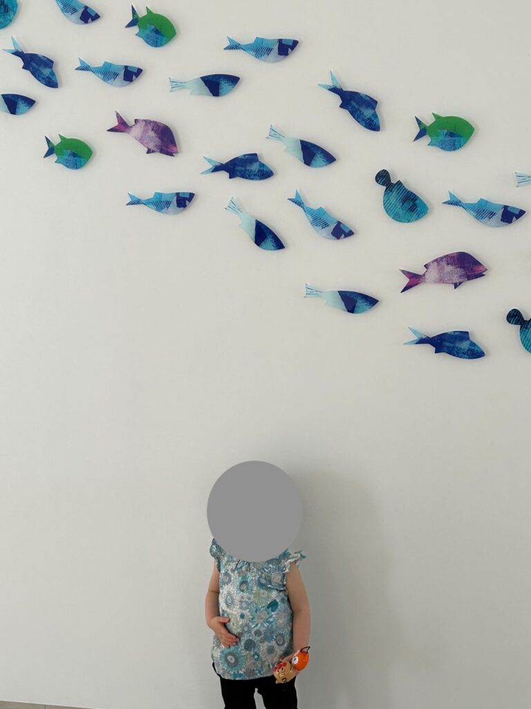 館内の魚の飾りの壁の前に立つ娘
